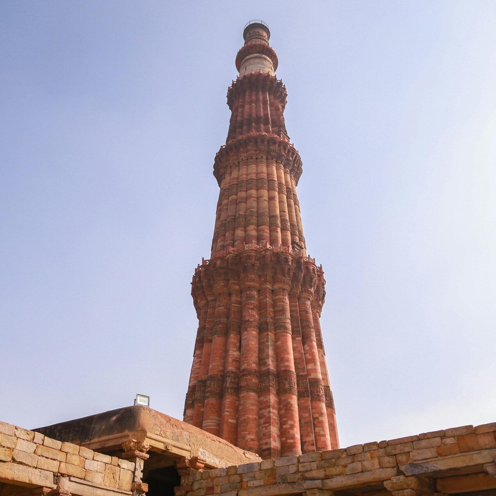 From below of ancient ornamental brick tower of Qutb Minar against cloudless blue sky located in historic complex in Delhi